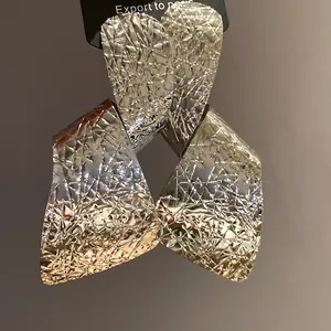 Close-up of oversized silver-tone earrings with irregular crinkled metal texture