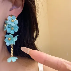 Close-up of light blue acrylic flower tassel earrings with gold chain on model's ear