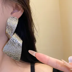 Detailed close-up showing the hammered texture of oversized irregular silver-colored earrings