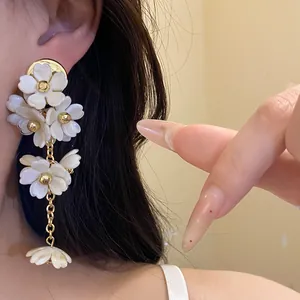 Close-up of elegant white acrylic flower tassel dangle earrings worn on ear.