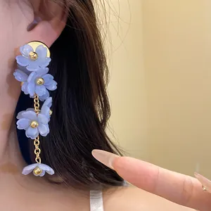 Close-up detail of elegant blue acrylic flower tassel earrings worn by a model