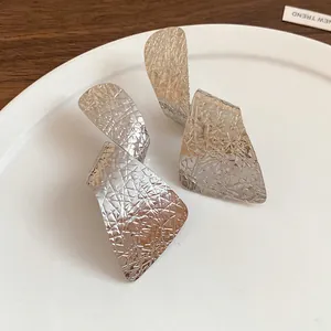 Close-up view of silver irregular textured metal drop earrings on a white ceramic plate