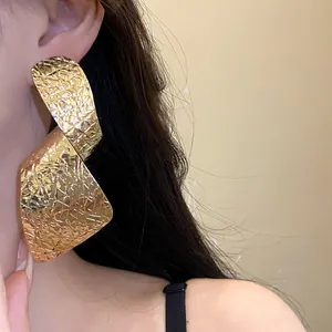 Close-up detail of exaggerated irregular crinkled gold long earrings worn by a model