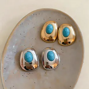 Close-up of gold and silver oval earrings with turquoise resin stones on a ceramic plate