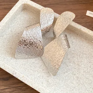 Macro view of textured silver irregular geometric earrings displayed on a stone tray
