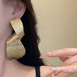 Close-up of large irregular textured gold earrings worn by an Asian model for fashion look