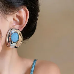 Detail of chunky geometric silver earrings with oval turquoise resin inlay on model