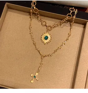 Dettaglio della collana a strati dorata con pendenti a forma di occhio e croce