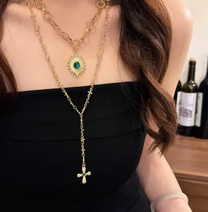 Primo piano di collana a strati in oro con pendenti a occhio solare e croce con pietre verdi