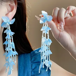 Nahaufnahme eleganter blauer Glasblumen-Ohrringe mit langen Quasten und feinen Perlendetails