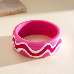 Close-up detail of a vibrant pink resin bangle featuring white and red wave patterns