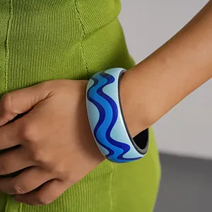 Blue wave patterned resin bangle worn with a green knit outfit for a vibrant look.