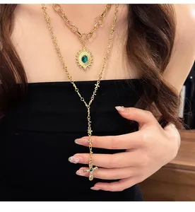 Dettaglio di una collana a croce dorata a strati con pietre verdi indossata da modella.