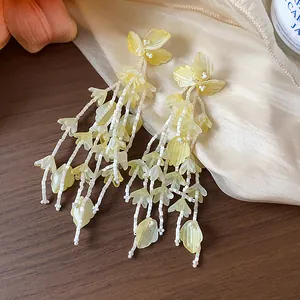 Elegante Nahaufnahme von gelben Glasblumen-Quastenohrringen auf Seidenhintergrund
