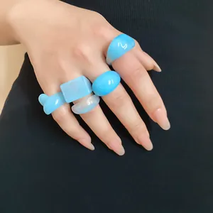 Macro view of several light blue resin geometric rings worn on a hand with black background