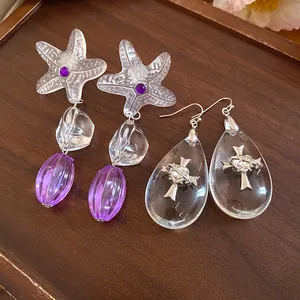 Detailed view of textured resin starfish and teardrop cross earrings on dark wood