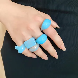 Close-up of hand wearing various blue resin geometric rings on black background