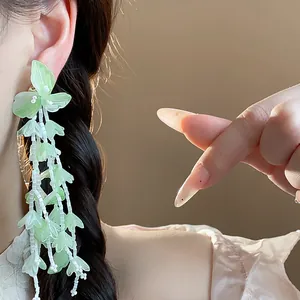 Detailansicht von grünen Glasblüten-Ohrringen am Ohr mit eleganten Perlenquasten