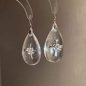 Detailed view of transparent resin teardrop earrings with silver cross and heart design.