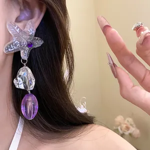 Detail view of irregular starfish pendant earring with purple resin beads on model.