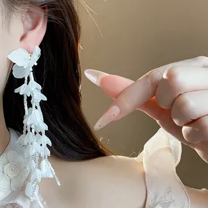 Nahaufnahme eleganter, 18 Karat vergoldeter weißer Glasblumen-Quastenohrringe an einem Modell.
