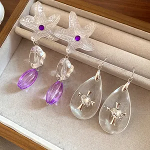 Detailed shot of unique resin starfish and teardrop cross earrings in a jewelry box