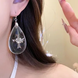 Close-up of a teardrop resin earring featuring a silver cross and heart detail on-ear.