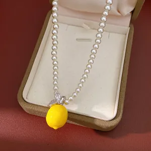 Gros plan d'un collier de perles avec pendentif citron jaune dans un écrin à bijoux