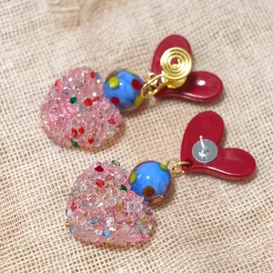 Detailed view of sweet heart-shaped earrings with pink crystals and red resin base