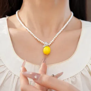 Détail d'un collier de perles avec pendentif citron en résine jaune et pierres de zircon