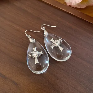 Detailed view of teardrop resin earrings featuring an intricate silver cross and heart motif