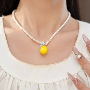 Gros plan d'un collier de perles avec un pendentif citron en résine jaune et zircone.