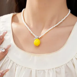 Gros plan d'un collier de perles blanches avec un pendentif citron en résine jaune vif et zircon