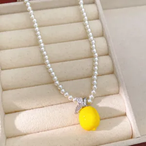 Gros plan d'un collier de perles avec pendentif citron en résine jaune et feuilles en zircon.