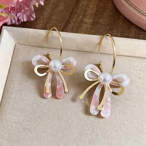Élégantes boucles d'oreilles nœud rose en forme de C avec perles blanches pour femme.