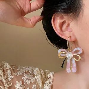 Élégantes boucles d'oreilles pendantes en résine rose et perles portées par un mannequin