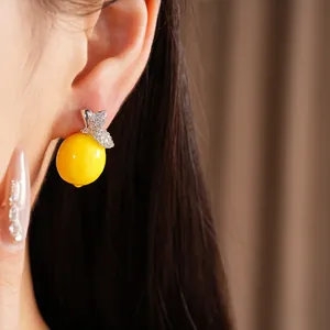 Gros plan d'une boucle d'oreille en résine jaune en forme de citron avec des zircons