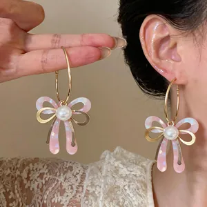 Élégantes boucles d'oreilles nœud rose avec perle centrale et monture dorée en anneau