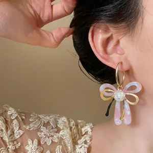 Gros plan élégant de boucles d'oreilles nœud rose et perle en forme de C portées.