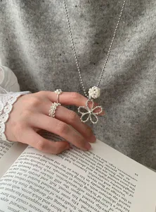 Close-up detail of a silver pearl flower necklace and woven rings on a grey sweater