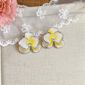 Dettaglio di orecchini a fiore in smalto bianco e giallo con pietra di zircone.