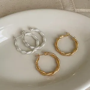 Detalle de pendientes de aro de metal retorcidos con un elegante acabado de textura mate