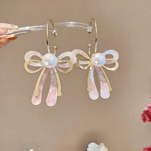 Vue détaillée des boucles d'oreilles nœud en marbre rose avec des perles et des créoles dorées