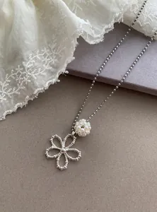 Close-up of silver-tone ball chain necklace with pearl bead and flower pendant details.
