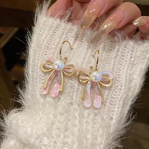 Gros plan détaillé de boucles d'oreilles nœud dorées avec acrylique rose marbré et perles