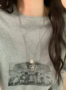 Detailed macro view of a delicate pearl flower pendant necklace worn on a grey t-shirt.