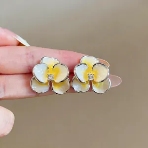 Dettaglio di orecchini a lobo a forma di fiore in smalto giallo e bianco con zircone