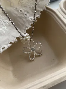 Close-up detail of a pearl bead cluster and hollow flower pendant on a ball chain necklace