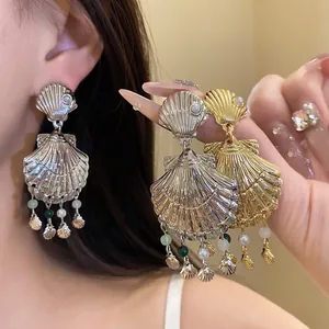 Vista de detalle de pendientes de borla con concha en acabado oro y plata para la playa