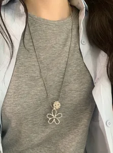Close-up of a stylish pearl flower pendant necklace worn on a grey ribbed sweater.